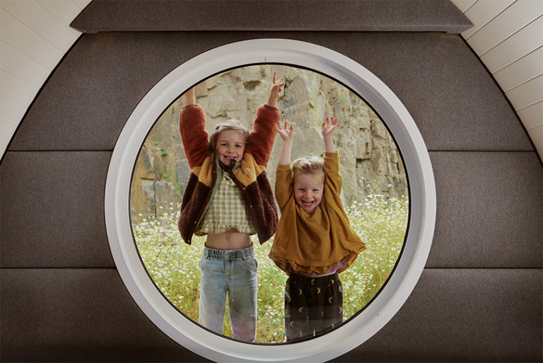 Two children playing viewed through a Lost Shore pod porthole